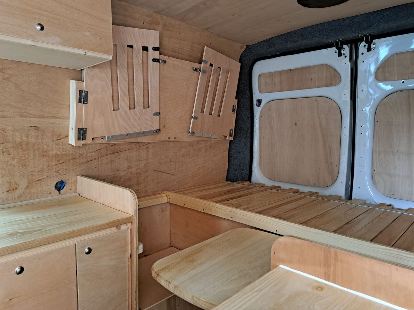 Campervan bed area carpentry with slatted base, fold-down cabinets and rear doors