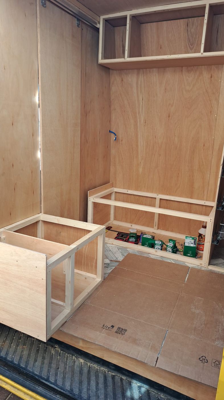 Campervan carpentry construction in progress — ply walls lined, timber bench frame and base cabinet boxes being built