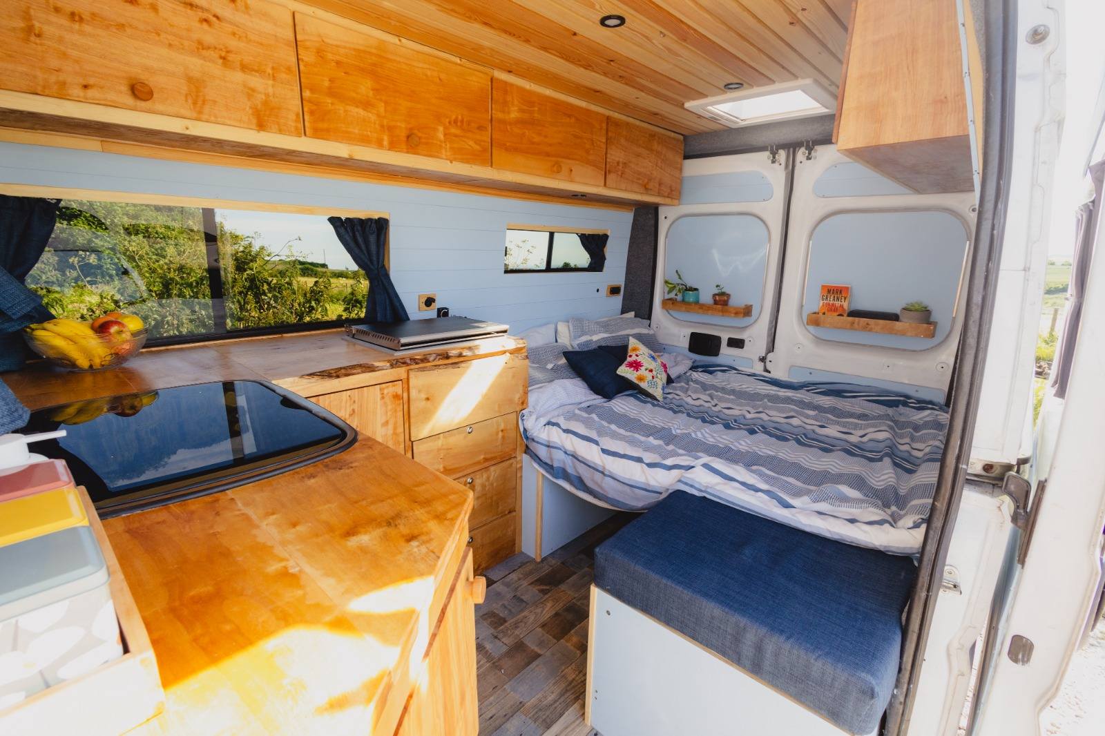 Finished campervan interior — bed and kitchen with countryside view through the window