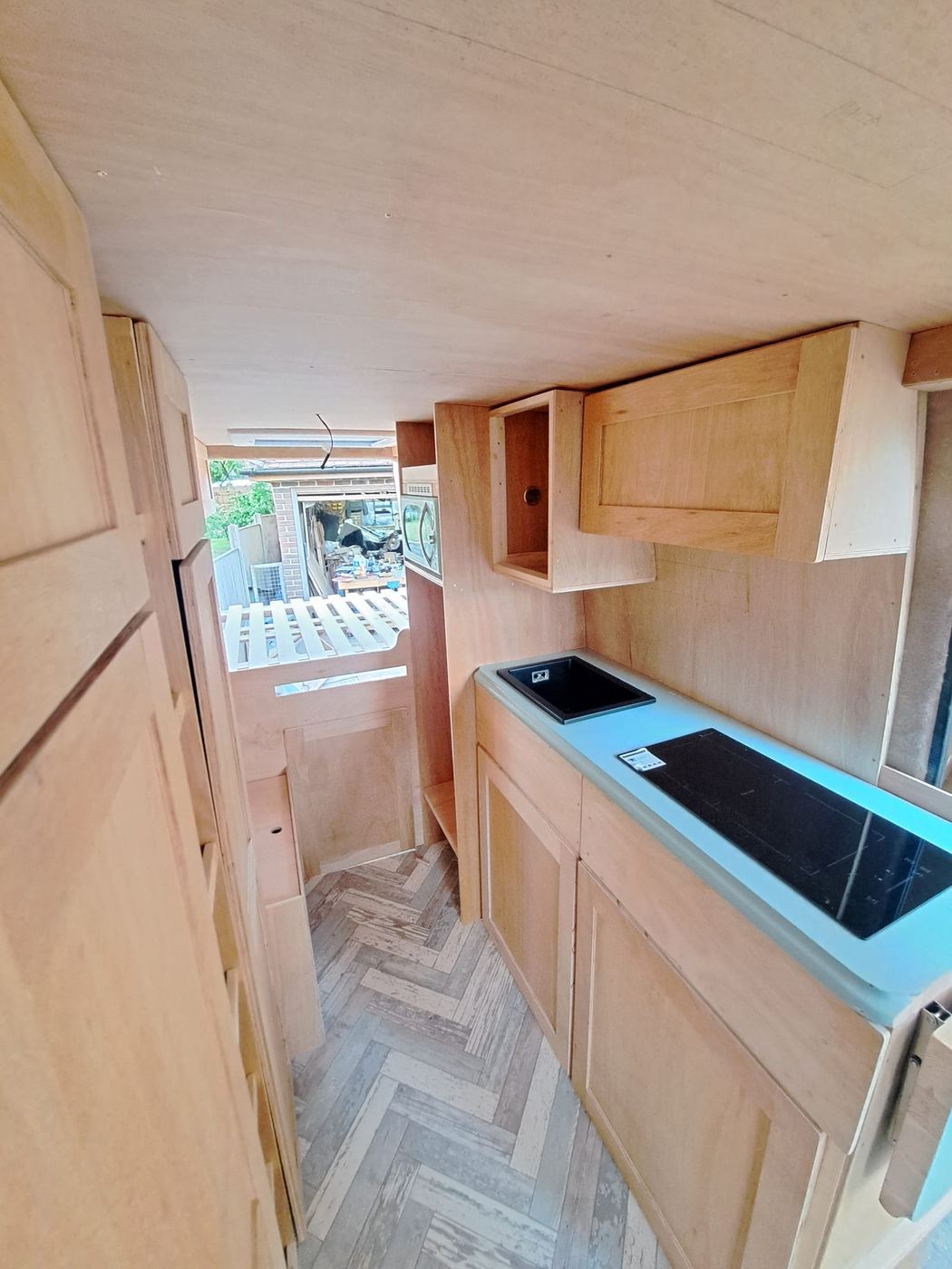 Finished birch ply kitchen carpentry — wall units, induction hob, sink, herringbone floor
